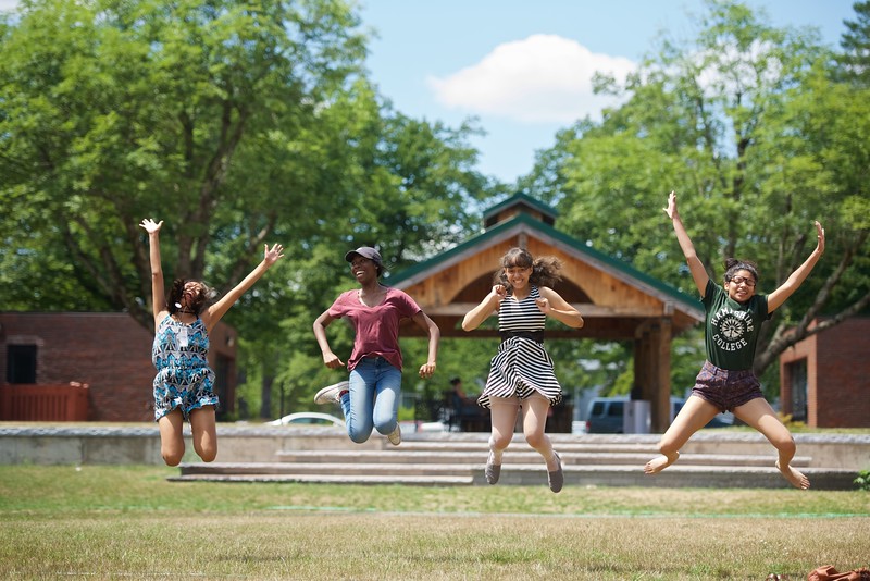 Four people jumping in a park. It is sunny and warm and they seem very happy.